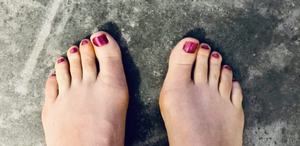 pretty pink pedicure on toes after a woman learned how to give herself a pedicure at home and remove calluses from her runner’s feet