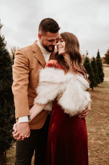 adorable and cute couple getting fall and winter engagement photo outside with woman in red velvet dress