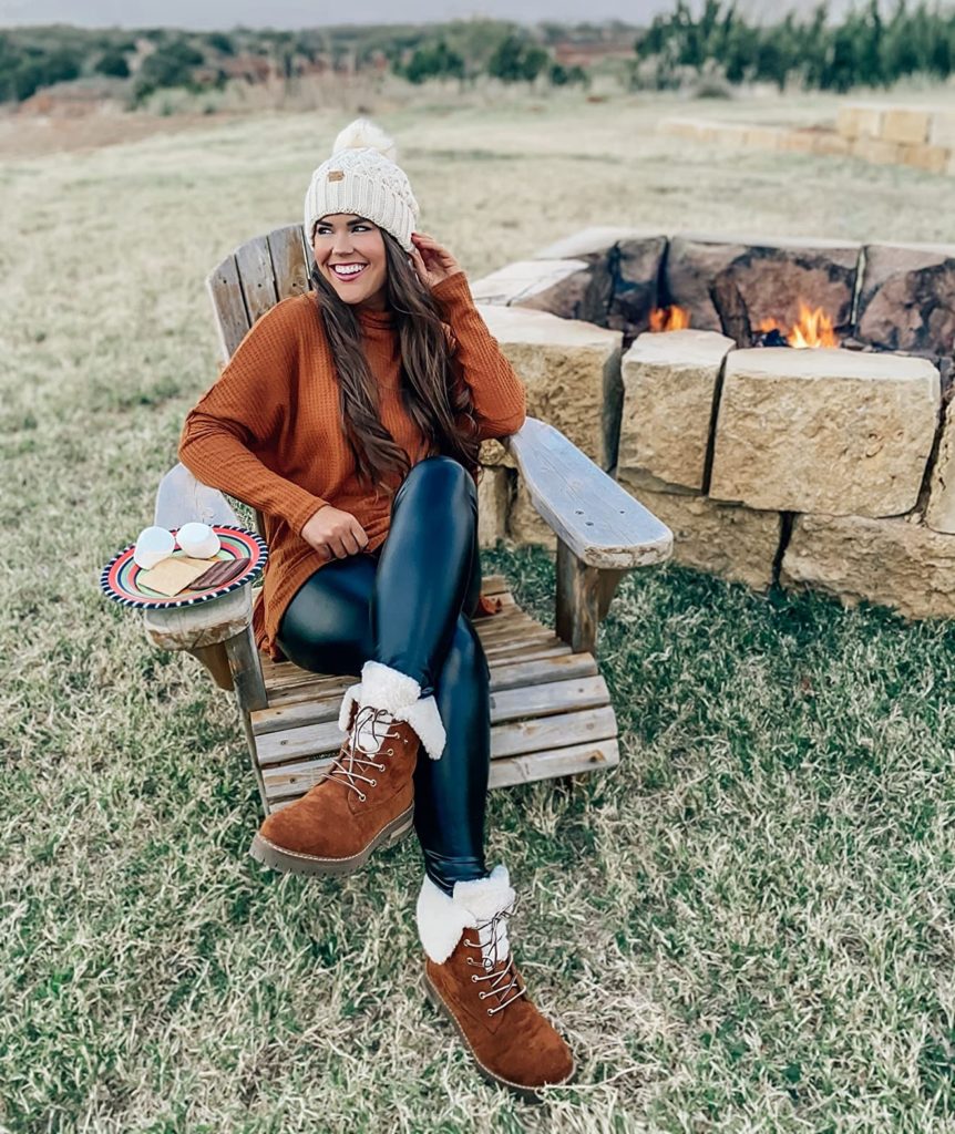 cozy winter outfit idea with black shiny leggings, hat, boots, and sweater
